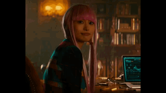 a woman in a pink wig is sitting in front of a laptop .