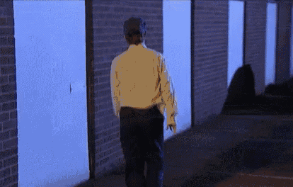 a man in a white shirt and black pants is walking in front of a row of blue doors .