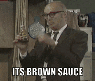 a man in a suit and tie is holding a bottle of brown sauce and saying it 's brown sauce