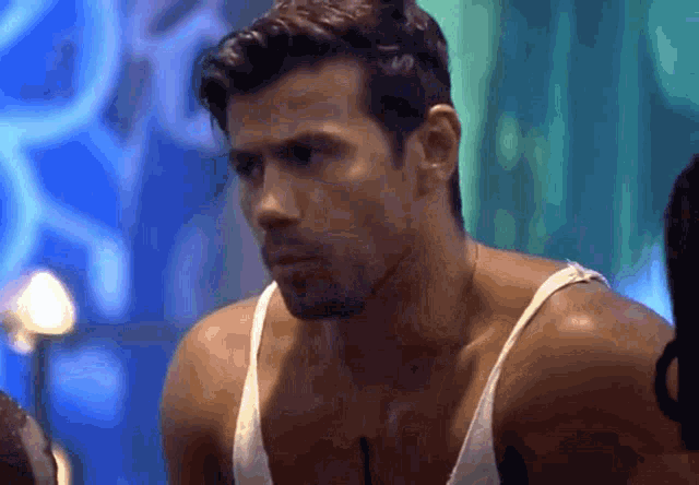 a man wearing a white tank top looks at the camera