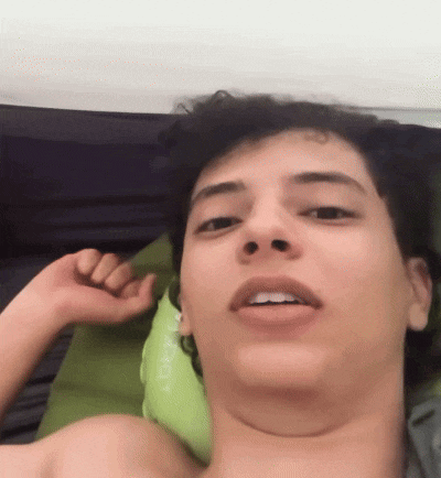 a shirtless man laying on a bed with a green pillow that says ' sherpa ' on it