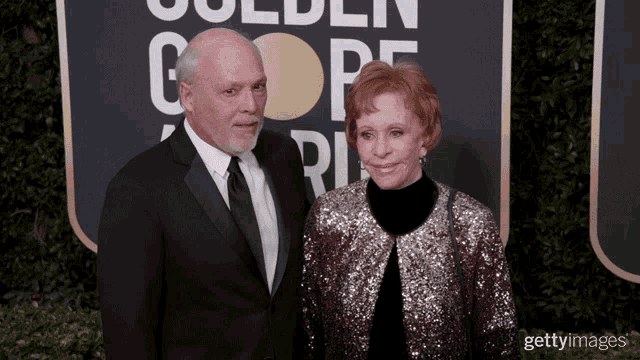 a man and a woman are standing on a red carpet in front of a golden globe sign