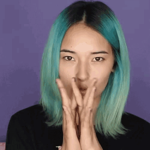 a woman with blue hair is making a funny face with her hands on her face .