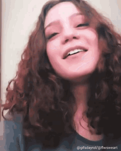 a woman with curly hair is smiling and wearing a blue shirt .