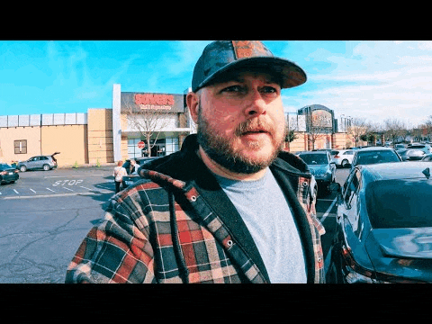 a man in a plaid shirt and hat is standing in a parking lot in front of a store called sanders