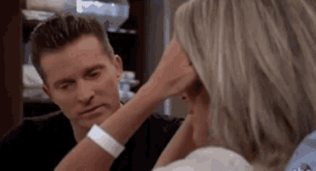 a man and a woman are sitting next to each other and the woman is touching the man 's head .