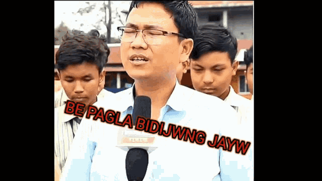 a man with glasses is speaking into a microphone with the words be pagla bidjwng jayw written on the bottom