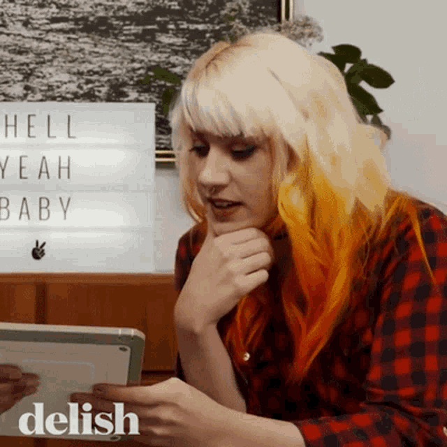 a woman looking at a tablet with a sign that says hell yeah baby in the background
