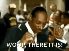 snoop dogg is wearing a suit and tie and is eating a sandwich .