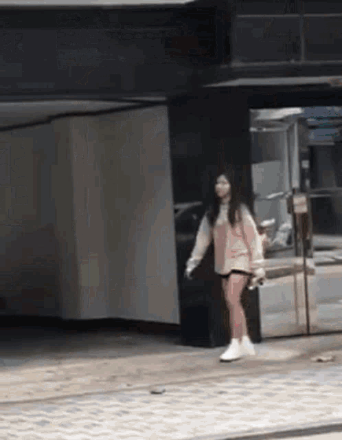 a woman in a pink sweater and white shorts is walking down a street