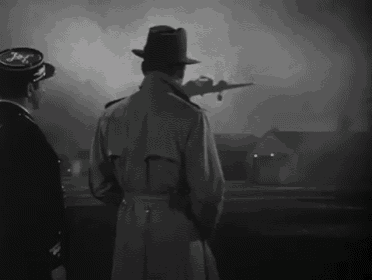 a man in a trench coat stands in front of a plane with the word jet on his hat