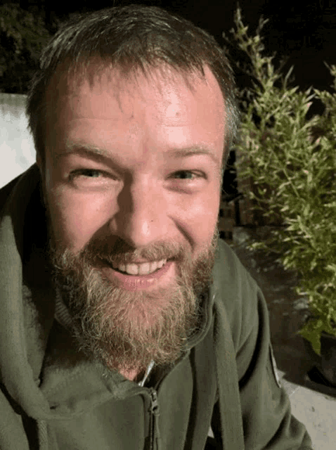 a man with a beard is smiling and wearing a green sweatshirt