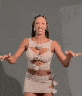a woman in a white dress is standing in front of a wall with her arms outstretched and smiling .