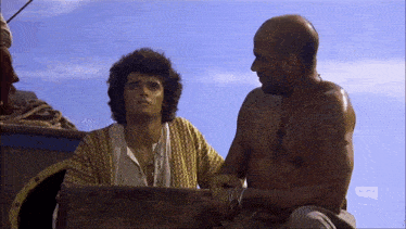 a shirtless man sits next to another shirtless man in front of a sign that says ' netflix ' on it