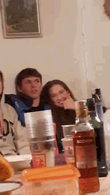 a group of people sitting around a table with a bottle of bozhov on the table