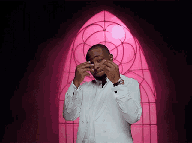 a man in a white suit is standing in front of a pink archway