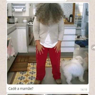 a woman with curly hair is standing next to a small white dog in a kitchen with the time 14:19