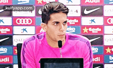 a man wearing a pink shirt is sitting in front of a microphone .