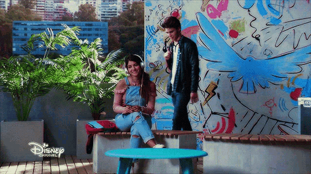 a man and a woman are standing in front of a disney channel mural