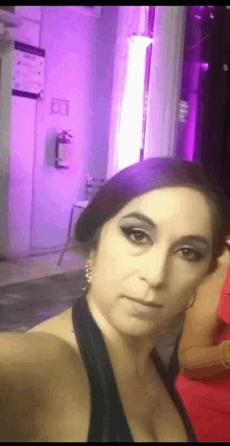 a woman in a black dress is taking a selfie in front of a purple wall .