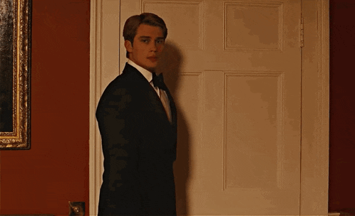 a man in a tuxedo and bow tie stands in a doorway