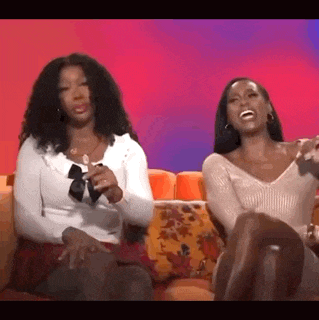 two women are sitting next to each other on a couch laughing .