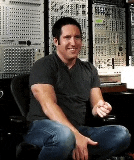 a man is sitting in a chair in front of a bunch of electronic equipment and making a funny face .