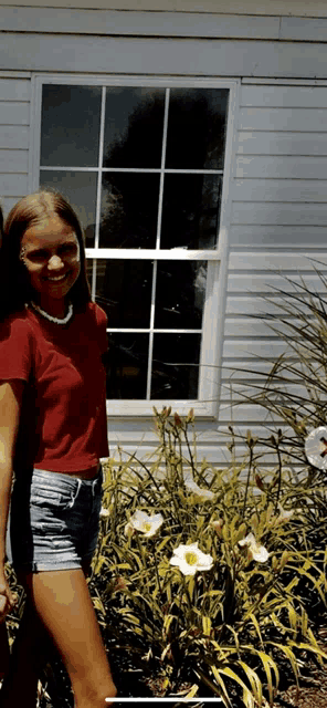 a woman in a red shirt and shorts is standing in front of a window