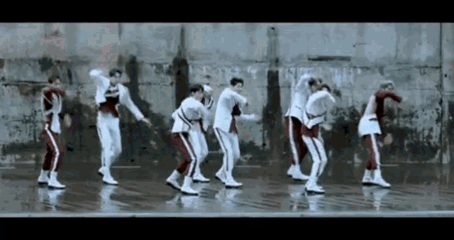 a group of young men are dancing in the rain in front of a concrete wall .