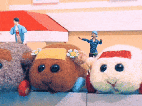 a stuffed animal with a yellow flower on its head sits next to a stuffed animal with a red hat