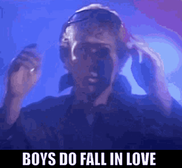 a man wearing headphones is dancing in a dark room with the words `` boys do fall in love '' above him .