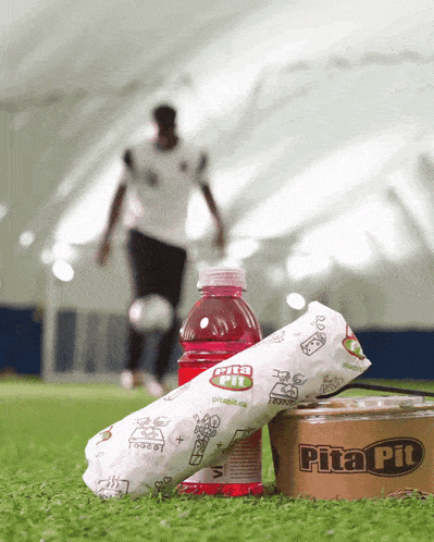 a man kicks a soccer ball in the background behind a pita pit container