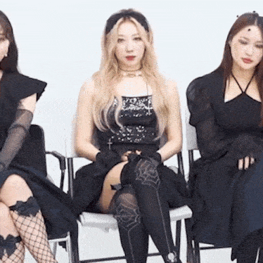 three women are sitting on chairs wearing black dresses and stockings .