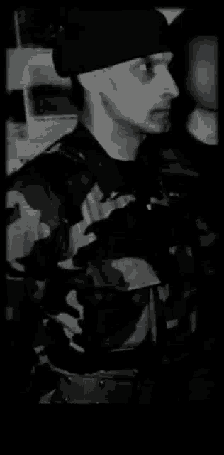 a black and white photo of a man wearing a hat and a camouflage shirt .