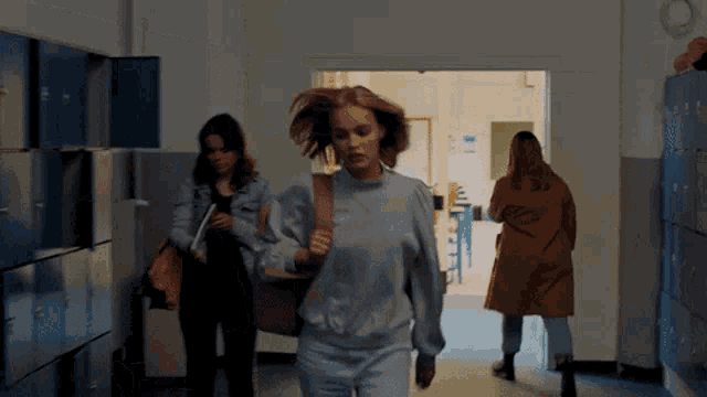 a woman walking down a hallway with lockers in the background