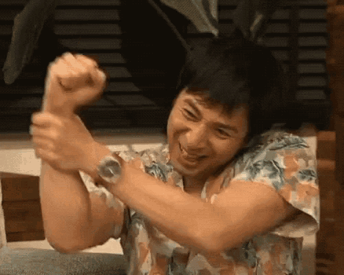 a man in a hawaiian shirt is holding his fist up in the air and smiling .