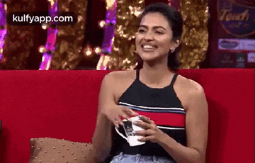 a woman is sitting on a couch holding a cup and smiling .
