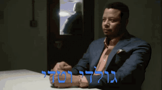 a man in a suit sits at a table in front of a sign that says ' goli '