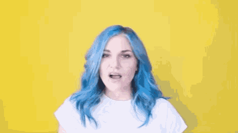 a woman with blue hair is wearing a white t-shirt and making a funny face .