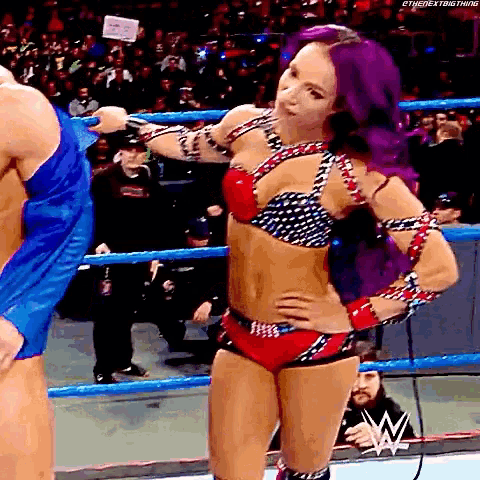 a woman with purple hair is standing in a wrestling ring with her hands on her hips .