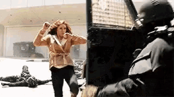 a woman is running away from a man in a helmet while a man watches .