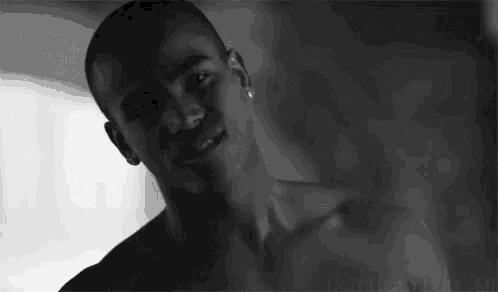 a black and white photo of a shirtless man with earrings on his ears .
