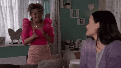 two women are sitting in a living room talking to each other .