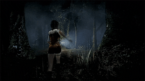a woman is walking through a dark forest in a video game .