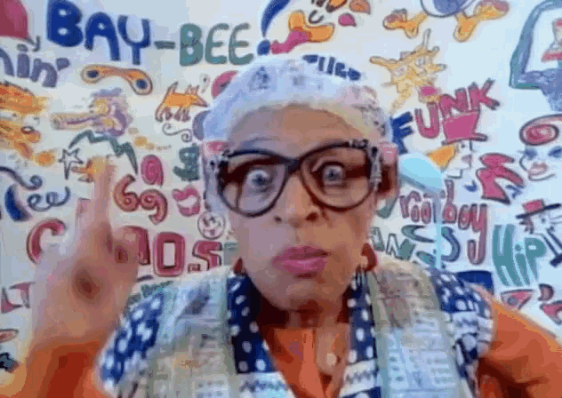 a woman wearing glasses stands in front of a wall that has the word bay-bee on it