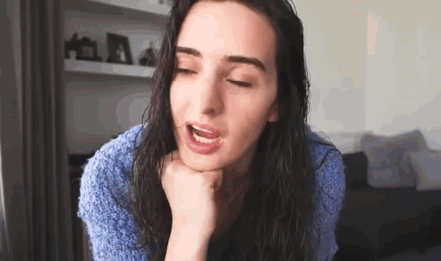 a woman in a blue sweater is sitting in a living room with her mouth open .