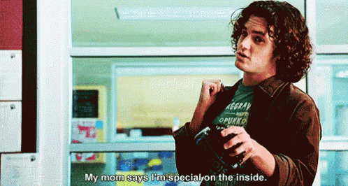 a young man with curly hair is standing in front of a window and says my mom says i 'm special