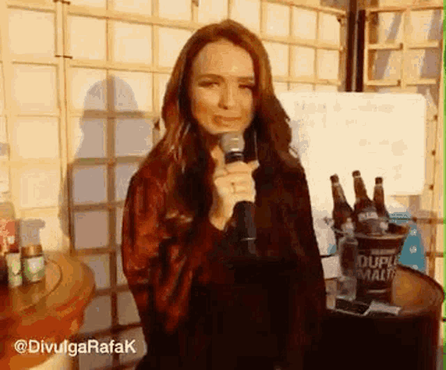 a woman is holding a microphone in front of a table with bottles of beer in it .