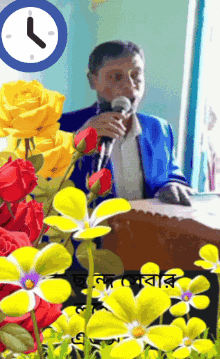 a man speaking into a microphone surrounded by yellow flowers and a clock