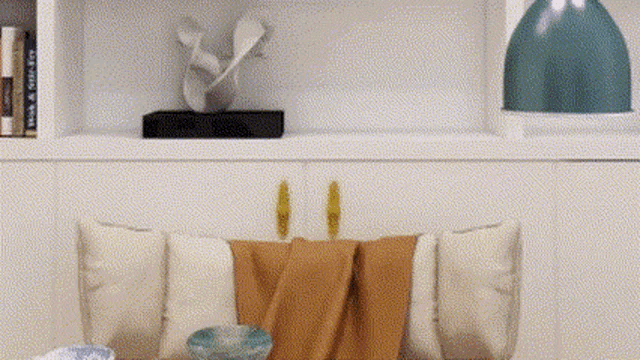 a living room with a couch and pillows and a shelf with a vase and a sculpture on it